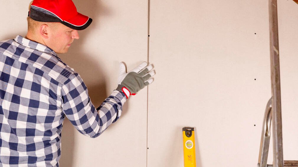 Construction worker holding gypsum board. Attic renovation. Installation of drywall Construction worker holding gypsum board. Attic renovation. Installation of drywall